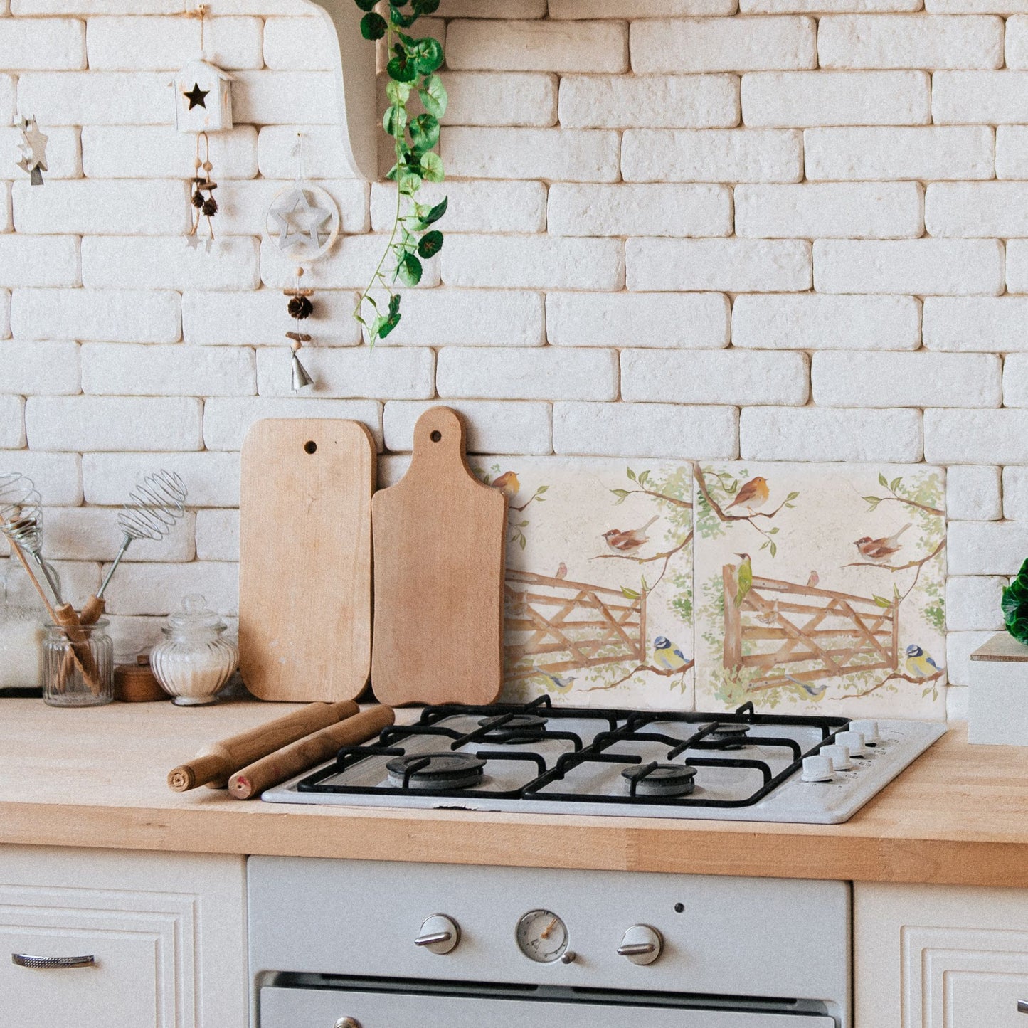 A tiled splashback behind an oven in a country farmhouse kitchen. The splashback is made up of large square cream marble tiles featuring countryside animals including British garden birds on a paddock gate.