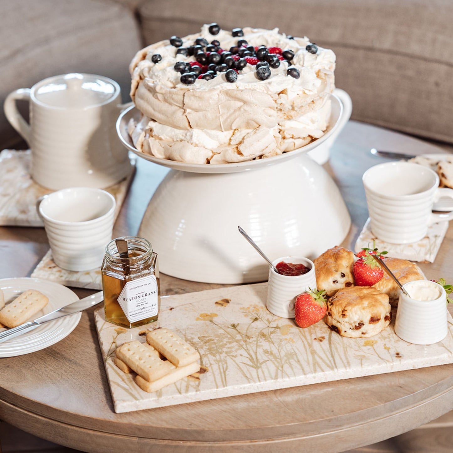 A rectangle marble sharing platter with a watercolour design featuring bees and a beehive in a buttercup meadow. The platter is being used to serve afternoon tea, including scones and jam.