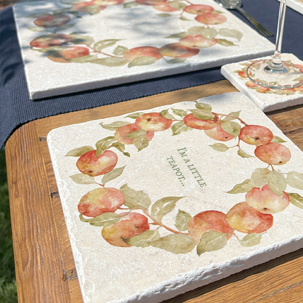 A medium marble serving board personalised with the customer’s choice of phrase: ‘I’m a little teapot…’. The serving board is set on a garden table next to a marble placemat in dappled shade.