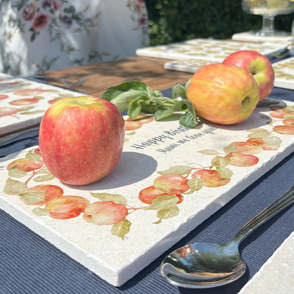 A personalised marble sharing board featuring a wreath of apples and leaves, with a bespoke message in the centre of the design. The personalised marble platter is placed on a sunny outdoor table.