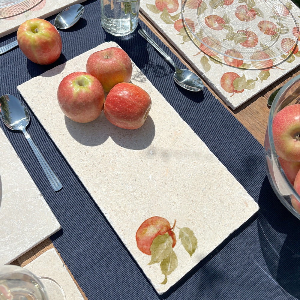 A garden table set with marble placemats and serving platters featuring a minimalistic apple watercolour design.
