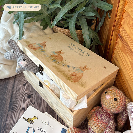 Large sized wooden pine personalised keepsake box. The design theme is perfect for New babies, Welcome to the world, baby showers and christenings. This design has baby bunnies, playing in a meadow style grass and a buzzy Bee flying around. The picture also shows an example in a nursey room filled with nappies, vests and teddys.