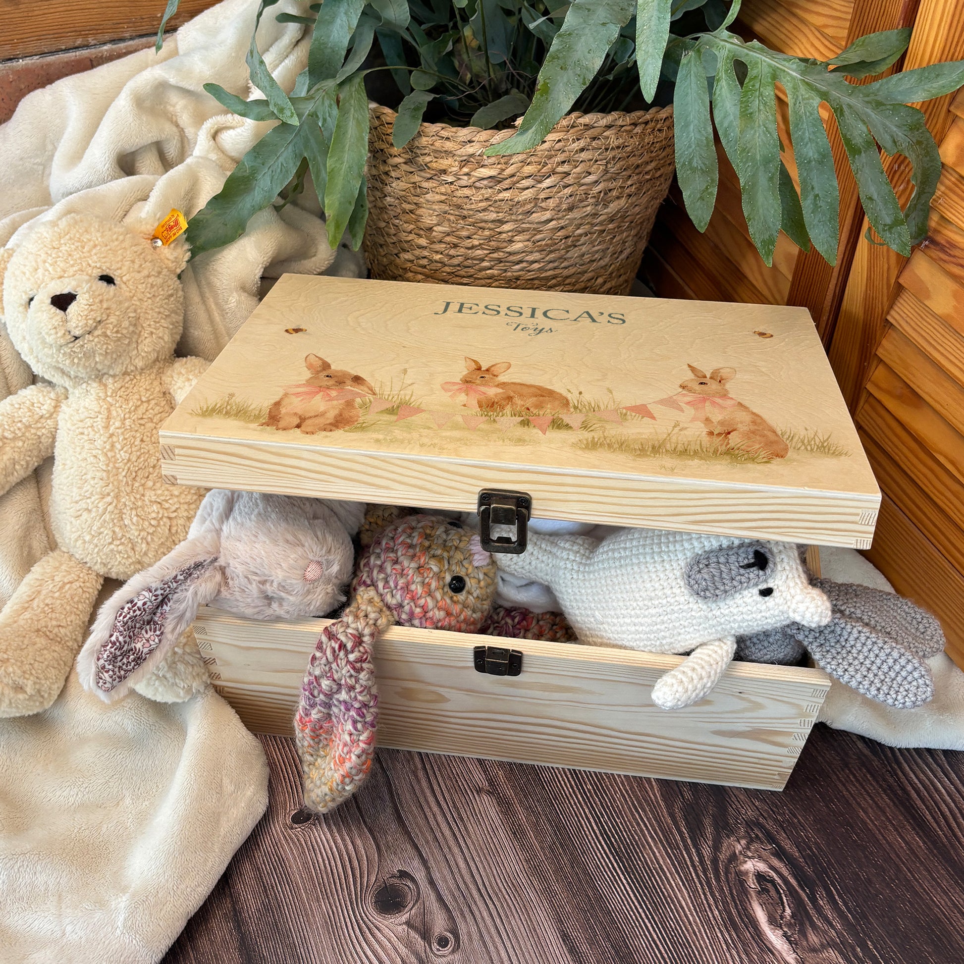 Large sized wooden pine personalised keepsake box. The design theme is perfect for New babies, Welcome to the world, baby showers and christenings. This design has baby bunnies, playing in a meadow style grass and a buzzy Bee flying around. The picture also shows an example in a nursey room filled with nappies, vests and teddys.