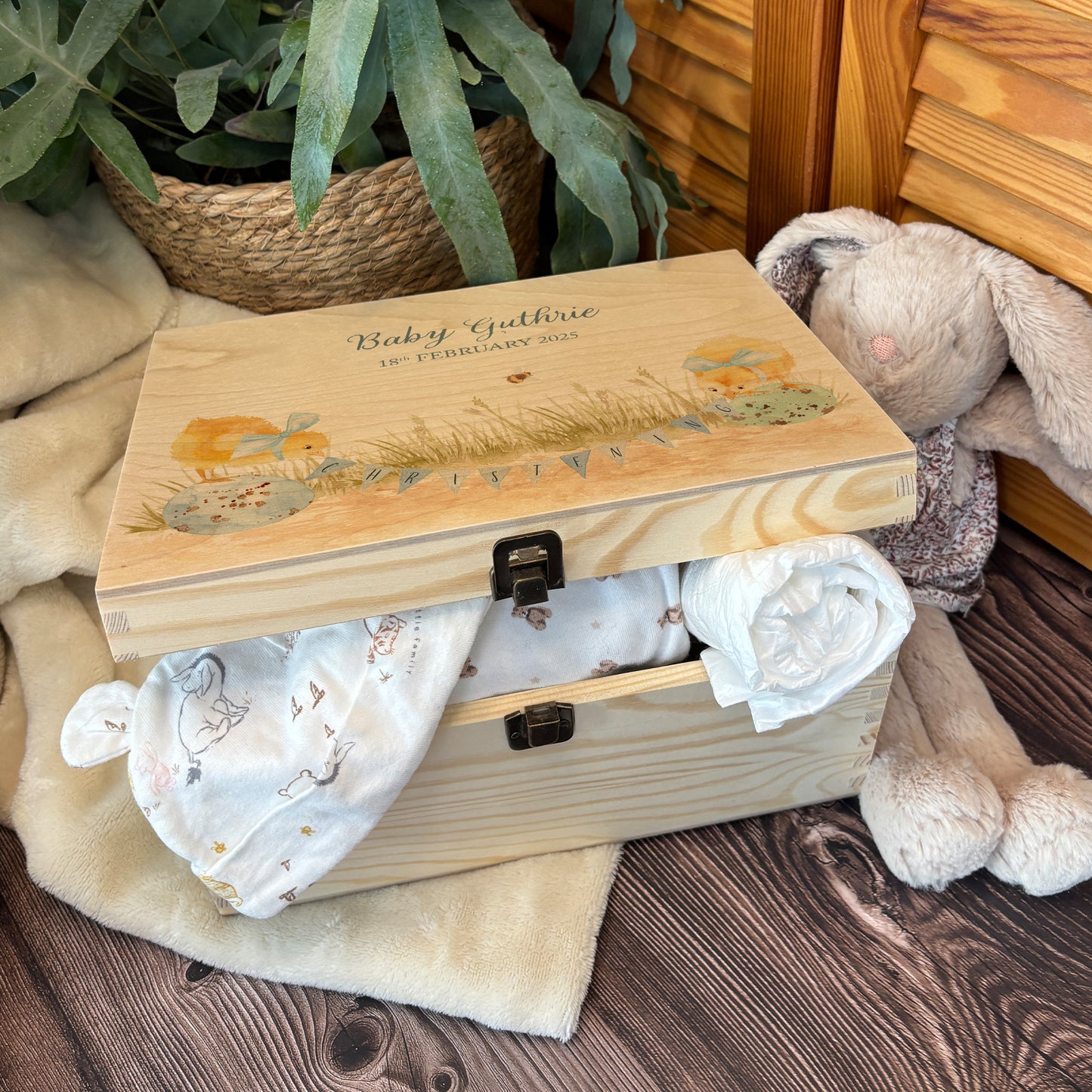 Medium sized wooden pine personalised keepsake box. The design theme is perfect for New babies, Welcome to the world, baby showers and christenings. This design has baby Chicks playing on some giant speckled eggs nestle in grass with a buzzy Bee flying around. The picture also shows an example in a nursey room filled with nappies, vests and teddys.