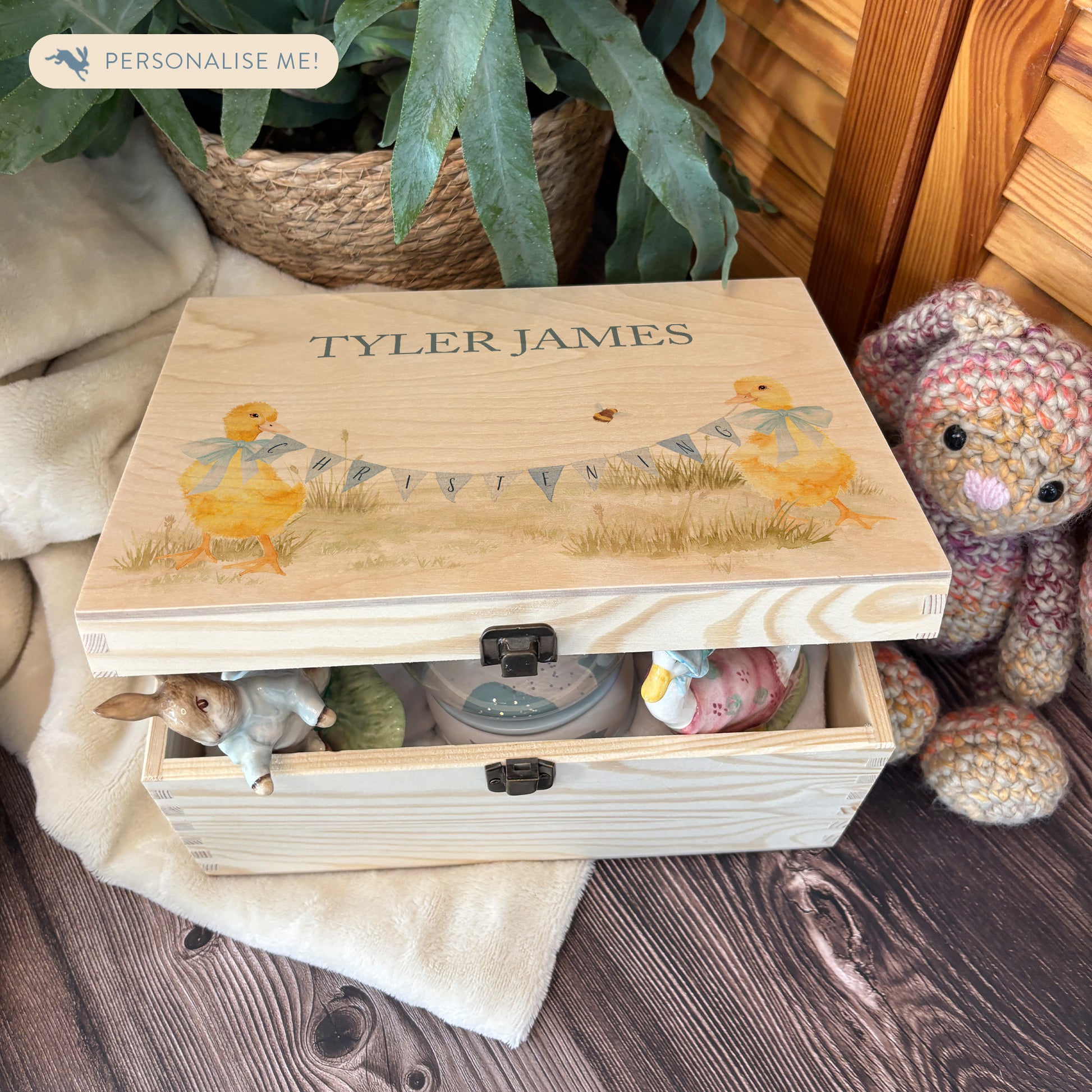 Medium sized wooden pine personalised keepsake box. The design theme is perfect for New babies, Welcome to the world, baby showers and christenings. This design has baby ducklings  in meadow style grass and a buzzy Bee flying around. The picture also shows an example in a nursey room filled with nappies, vests and teddys.