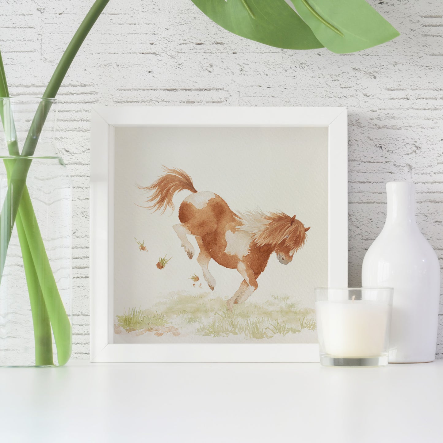 A framed greetings card with a watercolour design of a bucking Shetland pony in a field.