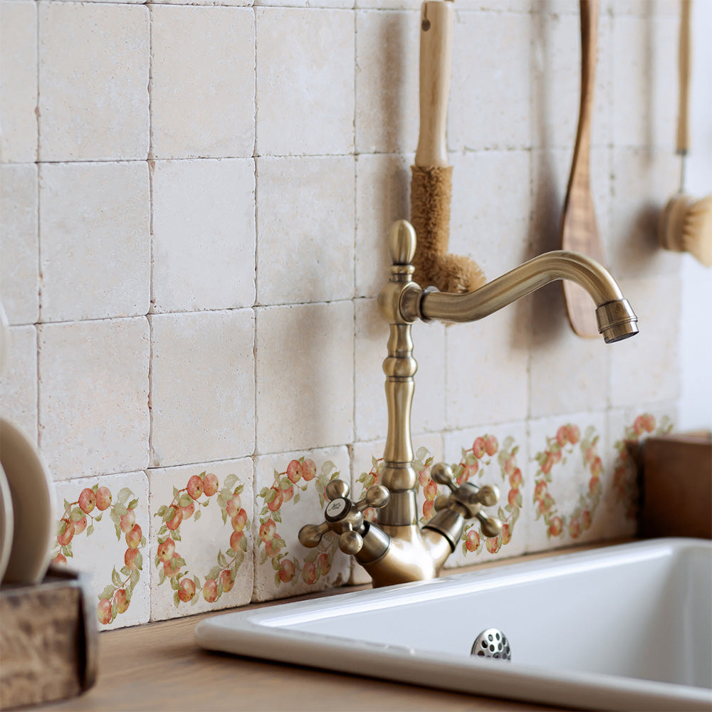 A farmhouse kitchen sink with a splash back made up of cream marble 10x10cm tiles with a watercolour apple wreath design.
