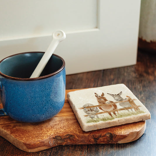 A square marble coaster with a design featuring three donkeys set on a kitchen worktop next to a coffee cup.