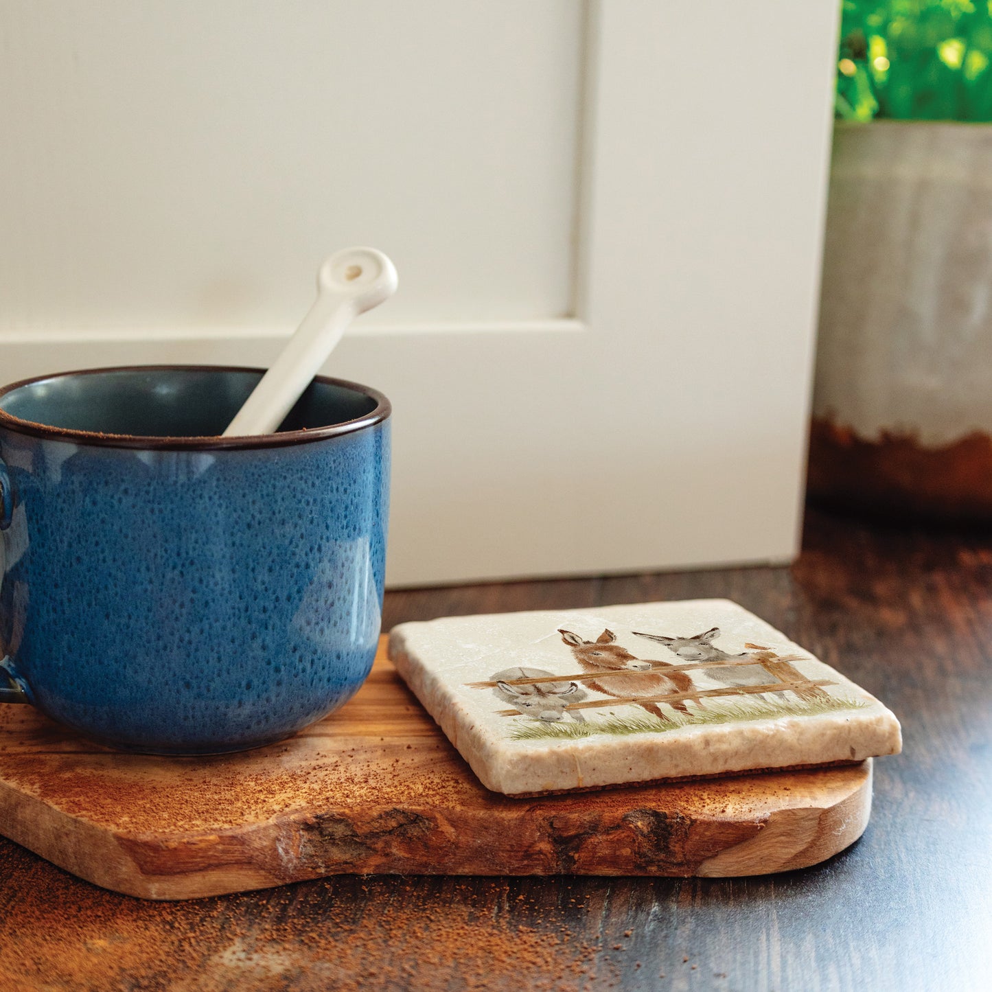 A handmade marble coaster with a design featuring three donkeys set on a kitchen worktop next to a coffee cup.