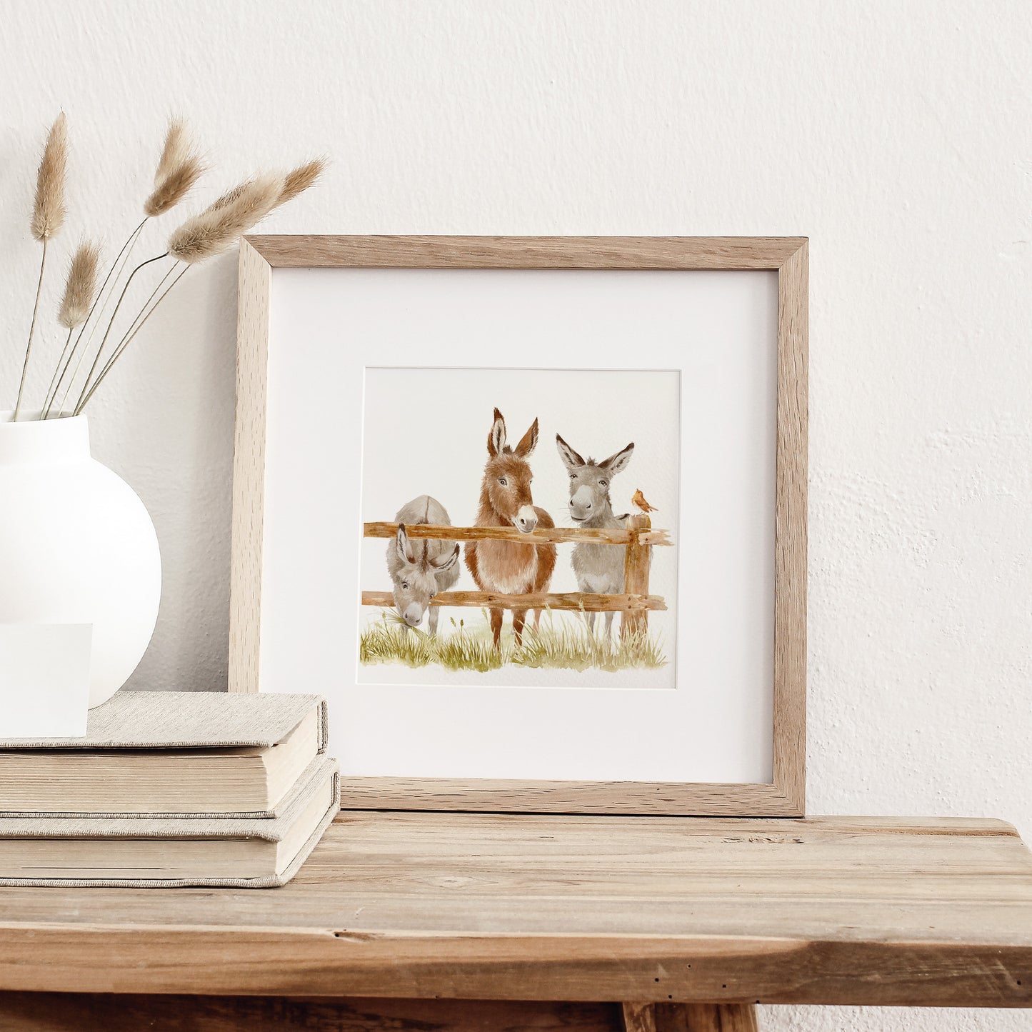 A framed bookmark greetings card featuring a watercolour scene of three donkeys peering over a wooden fence.