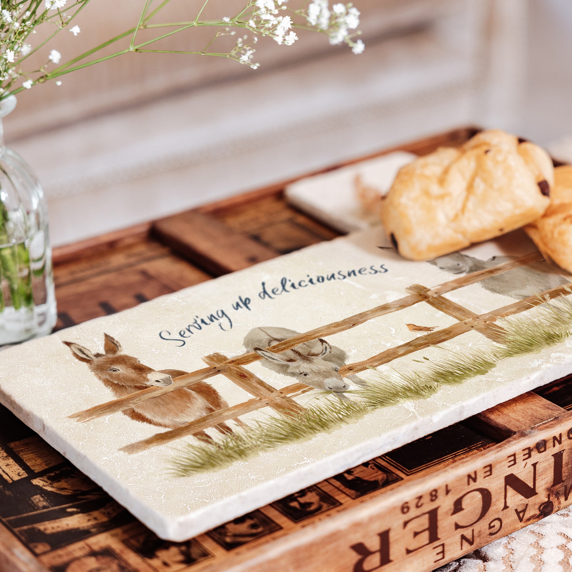 A personalised rectangular marble sharing platter featuring a herd of donkeys in a watercolour style. The example personalised blue text reads ‘Serving up deliciousness' in a brush script font.
