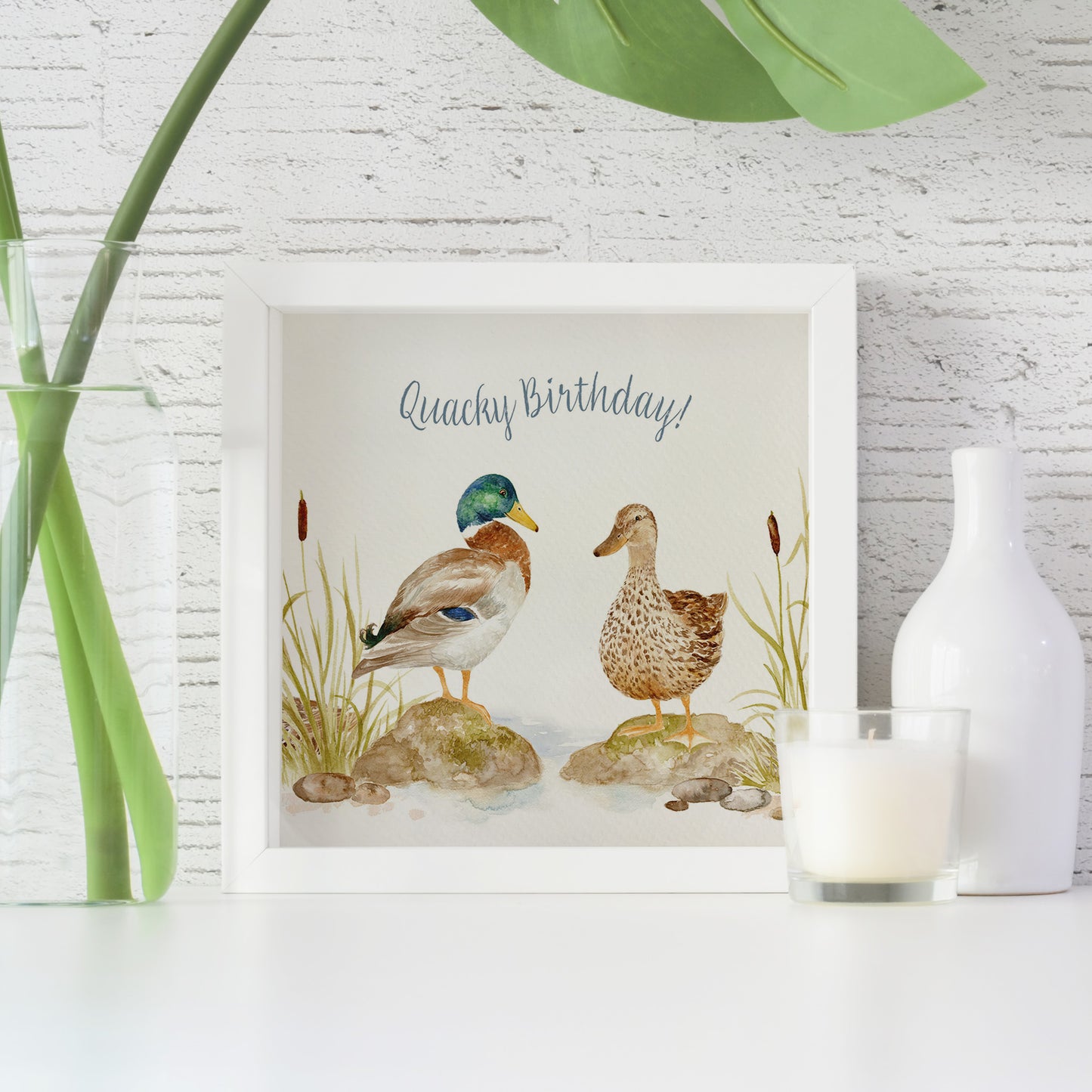 A framed greetings card featuring a watercolour design of two Mallard ducks that reads 'Quacky Birthday'.