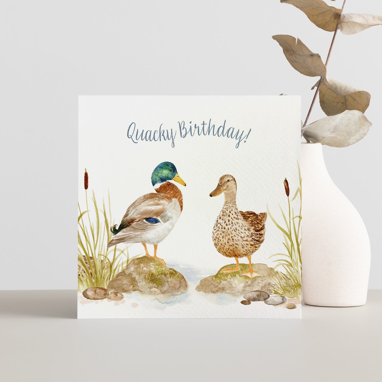 A square greetings card featuring a watercolour design of two Mallard ducks that reads 'Quacky Birthday'.