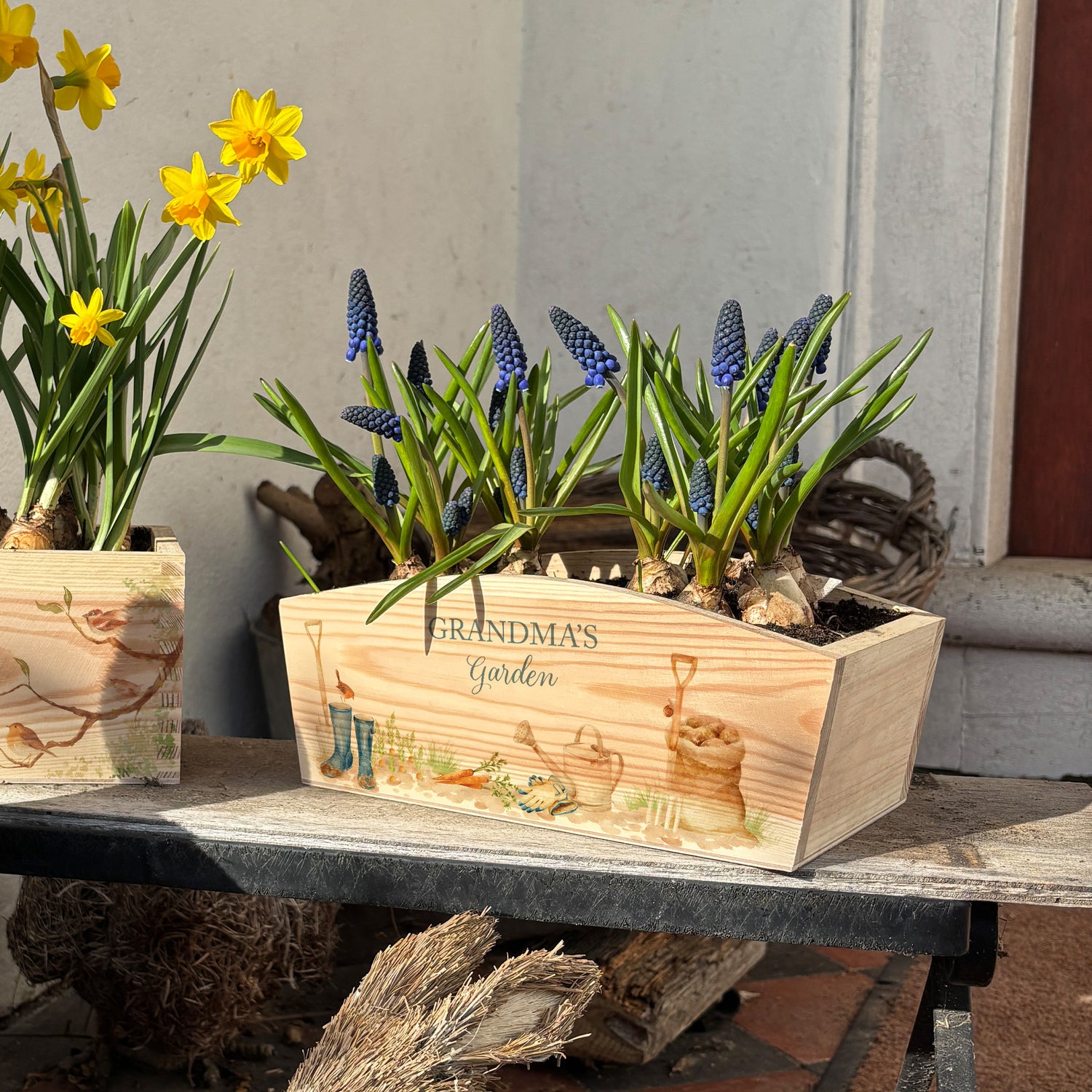 An arched wooden planter with a garden scene design, showing welly boots, a potato sack, a watering can and garden fork and spade. The planter is personalised with a special message. A perfect gift for gardeners.