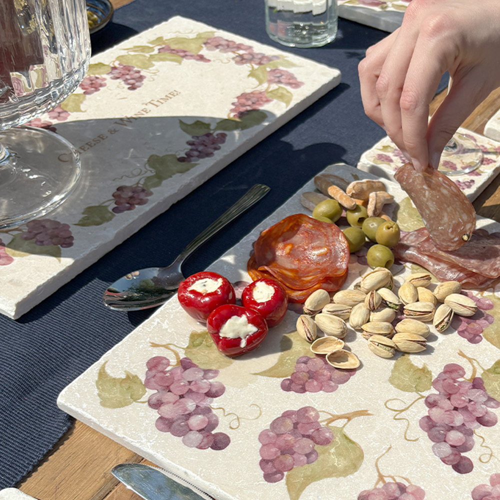 A personalised marble sharing board featuring a wreath of grape vines and leaves, with a bespoke message in the centre of the design. The personalised marble platter is placed on a sunny outdoor table.