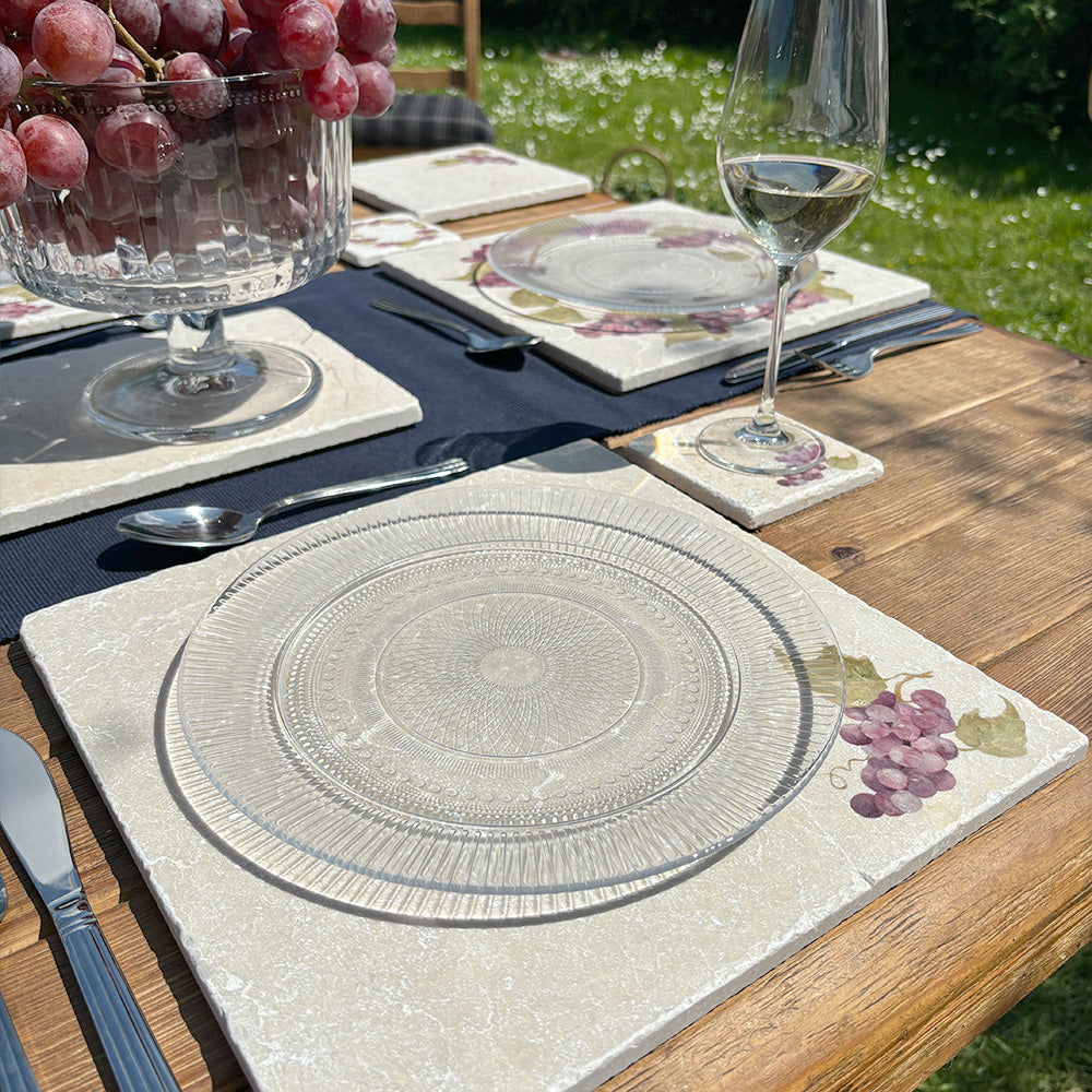 A garden table set with large square marble placemats featuring a minimalistic grape vine design.