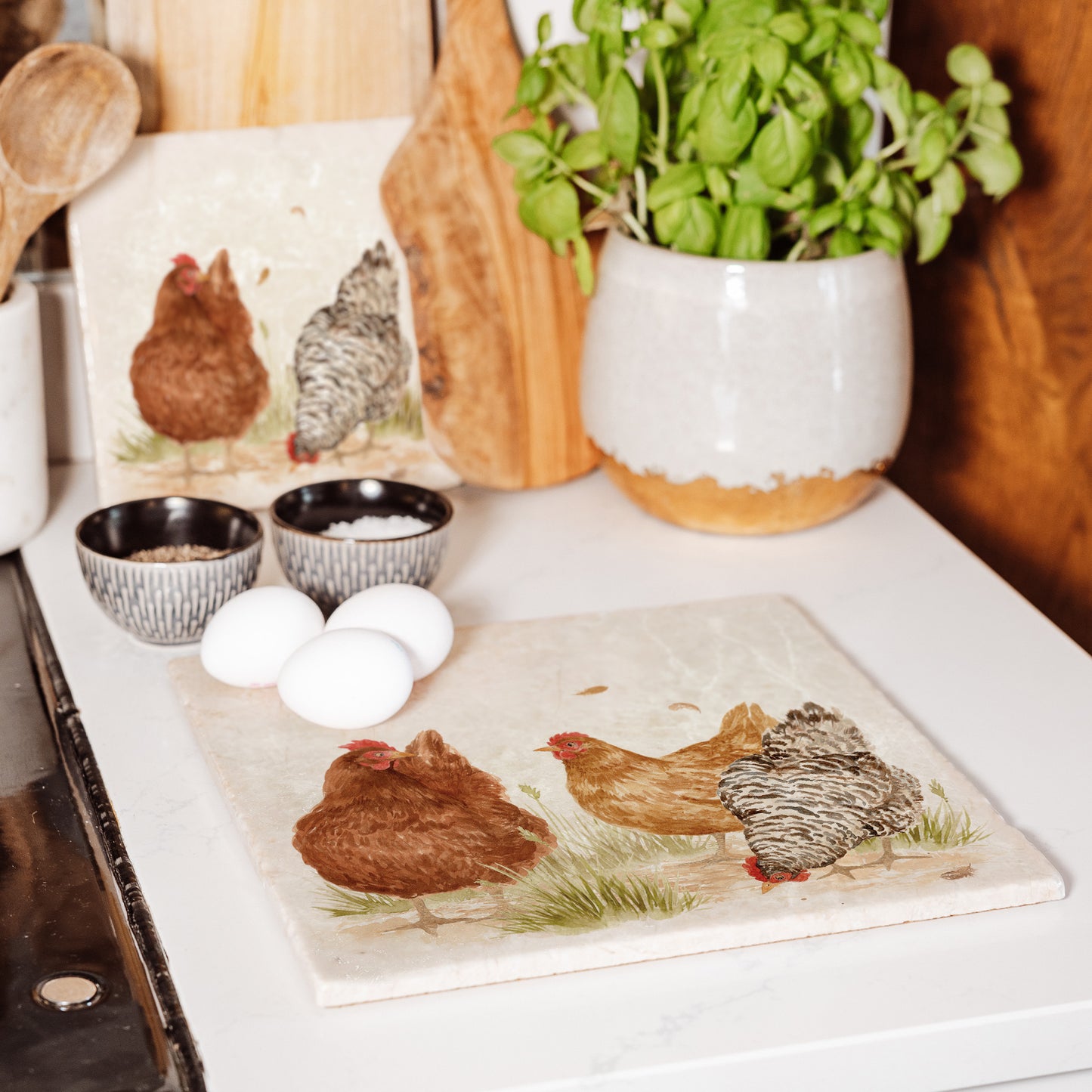 A large square marble platter featuring a watercolour hens design. The platter is set on a kitchen worktop next to the hob to be used as a worktop saver.