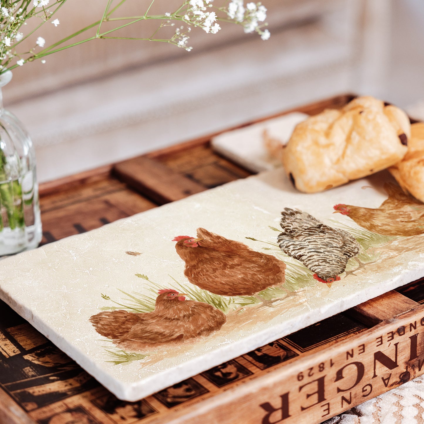 A rectangle marble sharing platter being used to serve breakfast pastries. The platter has a watercolour design featuring four hens in a farmyard.