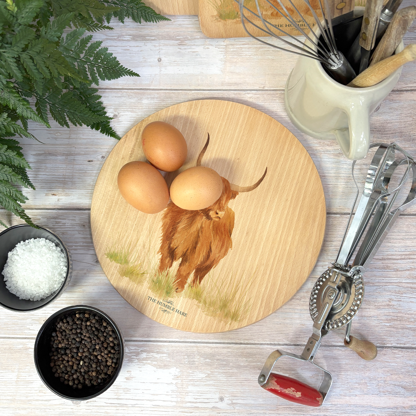 Handmade wooden chopping board featuring a watercolour Highland cow illustration, tied with blue ribbon.