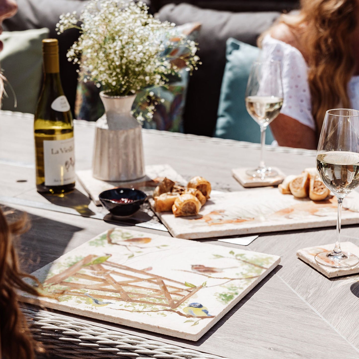 A garden table set with multipurpose marble platters for al fresco dining. A large marble platter features a watercolour design of British garden birds in the hedgerow around the paddock gate.