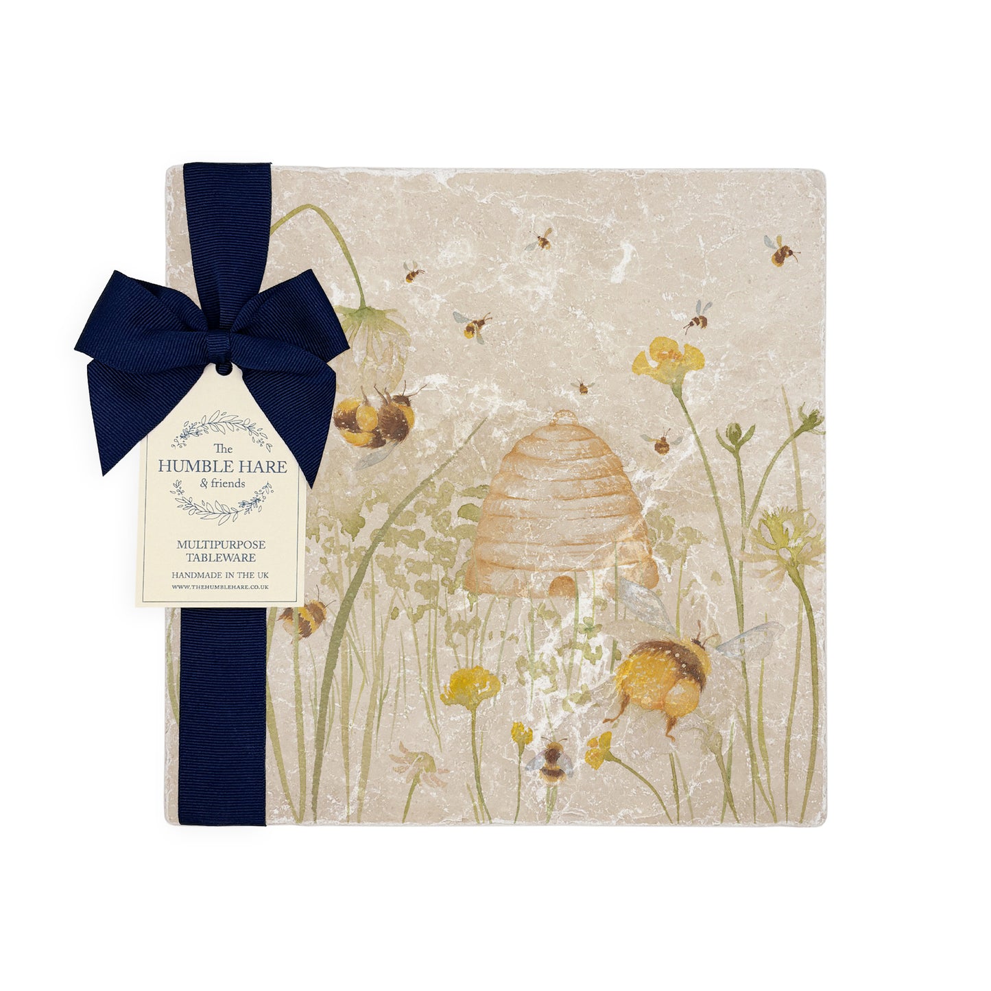 A multipurpose marble platter with a watercolour design featuring bees and a beehive in a buttercup meadow, packaged with a luxurious dark blue bow and branded gift tag.