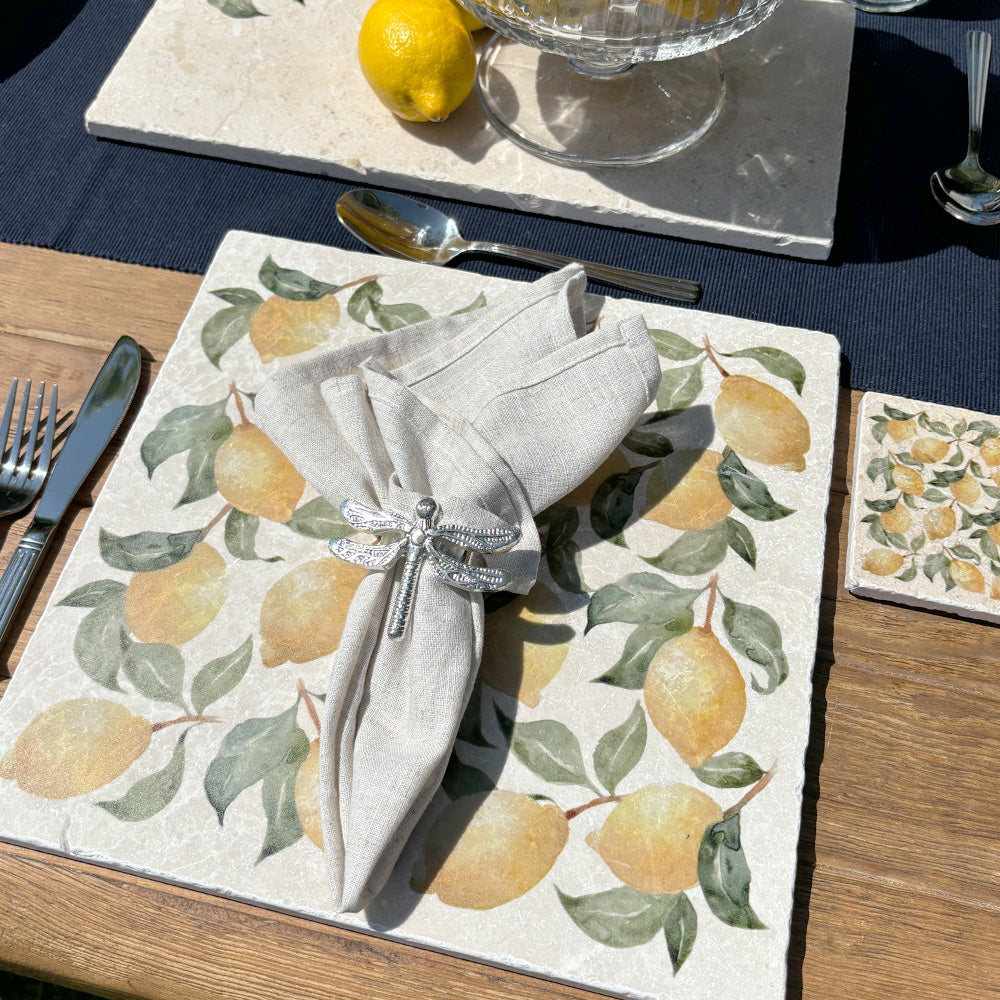 An al fresco dinging table set with marble placemats and coasters featuring a maximalist lemon pattern.