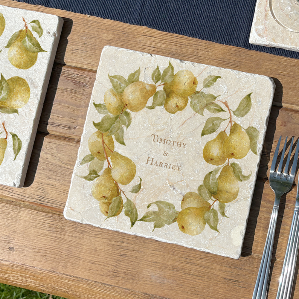 A medium marble serving board personalised with the customer’s choice of names. The serving board is set on a garden table next to a marble placemat in the sunshine.
