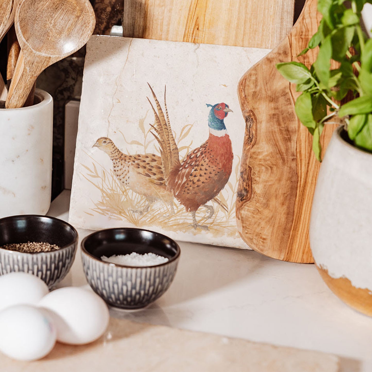 A medium square marble chopping board, featuring a watercolour design of a pair of pheasants, one male and one female, in golden grass.