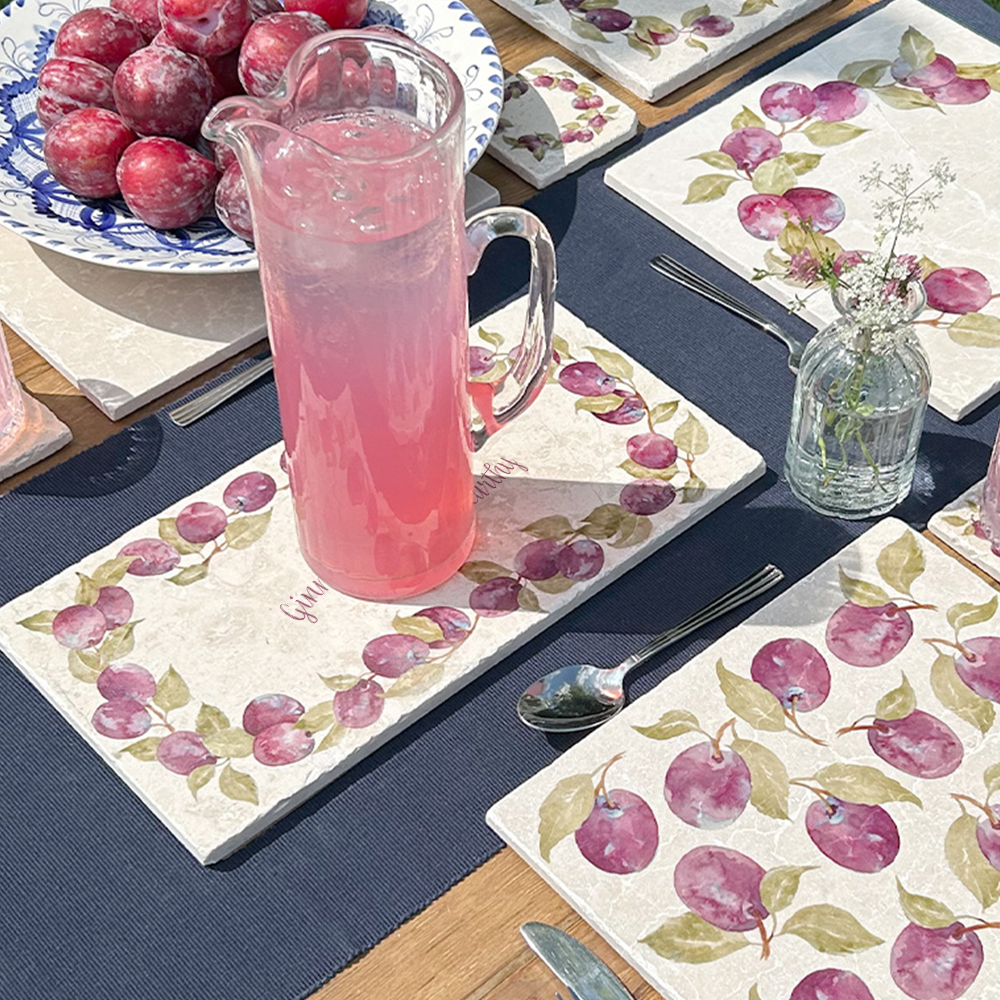A personalised marble sharing platter featuring a wreath of plums and leaves, with a bespoke message in the centre of the design. The personalised marble platter is placed on a sunny outdoor table.