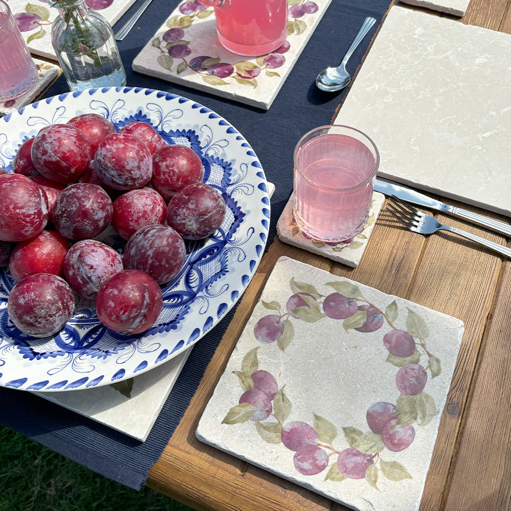 A medium square marble platter featuring a watercolour plum wreath design. The platter is set on a dinner table next to a marble placemat and coaster.