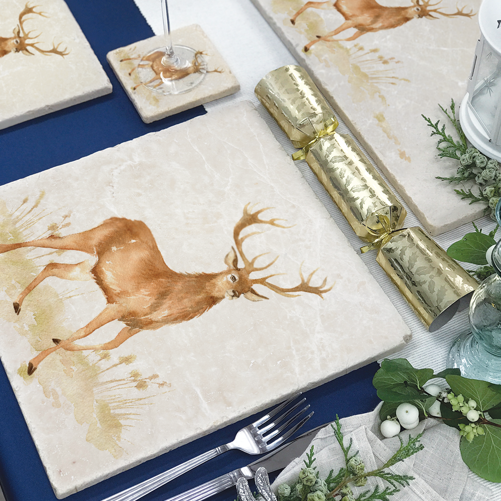 A handmade marble placemat featuring a noble stag in a watercolour style. The placemat is laid on a table set for Christmas dinner.