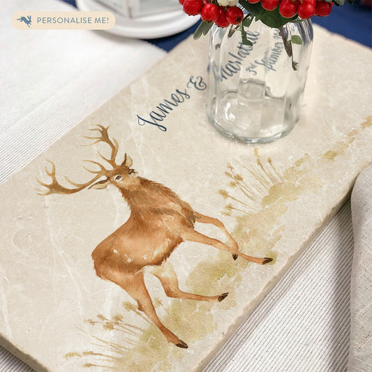 A personalised marble sharing platter set as a centrepiece on a festive dining table. The platter features a stag in a watercolour style, and the platter is personalised with dark blue text in a calligraphic style.