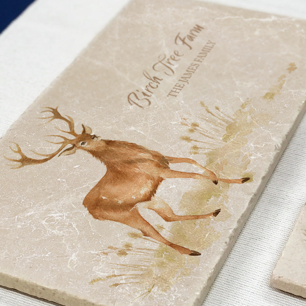 A marble sharing platter with a stag design set on a dining table. The platter is personalised with the family name and name of their house in neutral colour text.