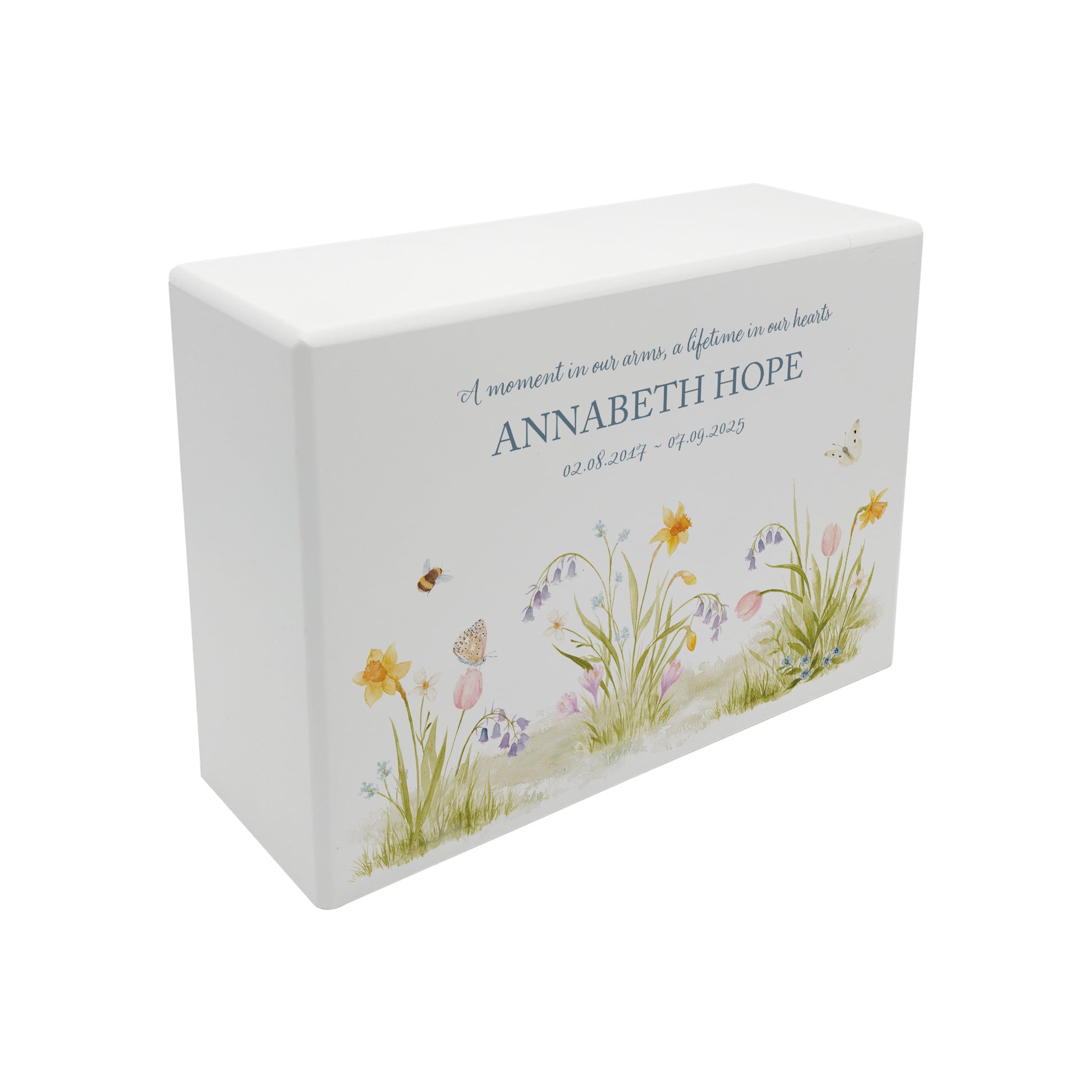 A beautifully crafted solid wooden urn, finished in white with a soft watercolour design with Spring flowers, Bees and Butterflies,. Thoughtfully made for either display or burial, this personalised urn can be customised to create a meaningful memorial. Perfect for holding ashes of a loved one or a beloved pet, it serves as a comforting tribute and keepsake.