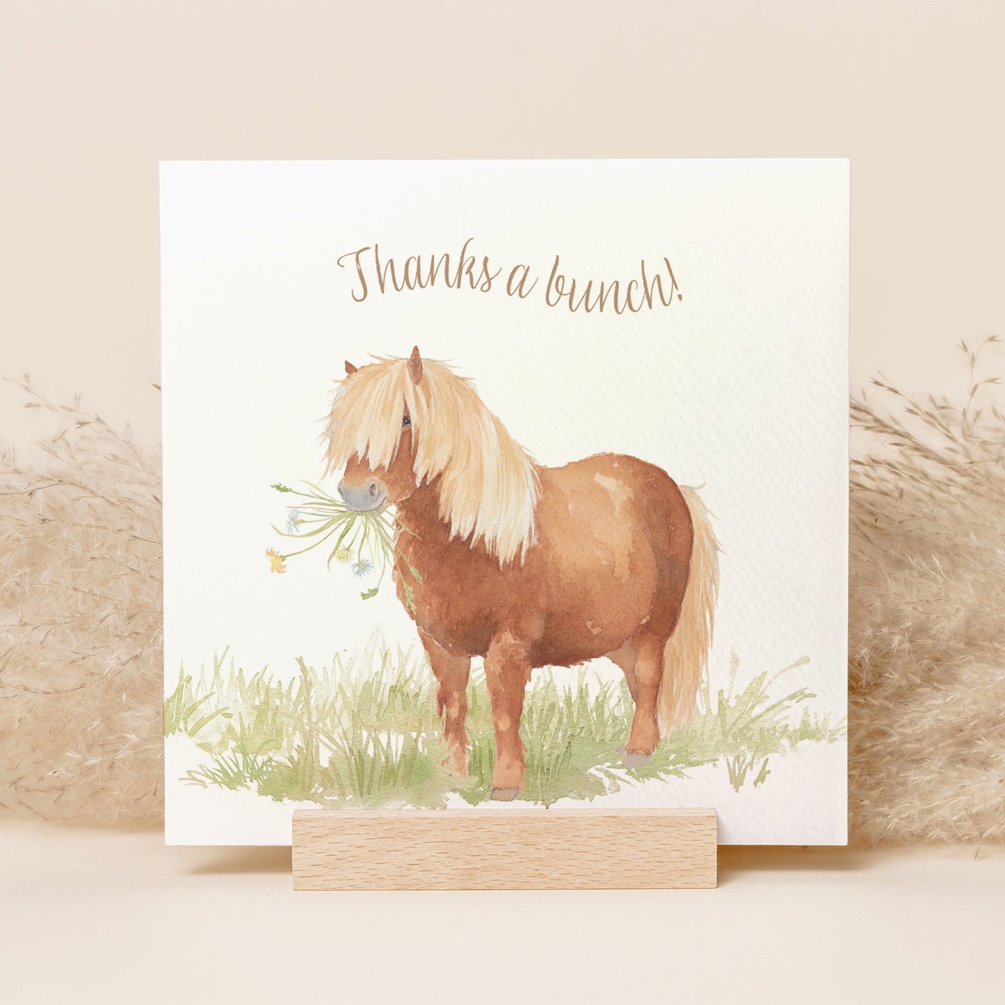 A greetings card reading Thanks a Bunch in brown text above a chestnut Shetland pony holding a bunch of flowers in a watercolour style.