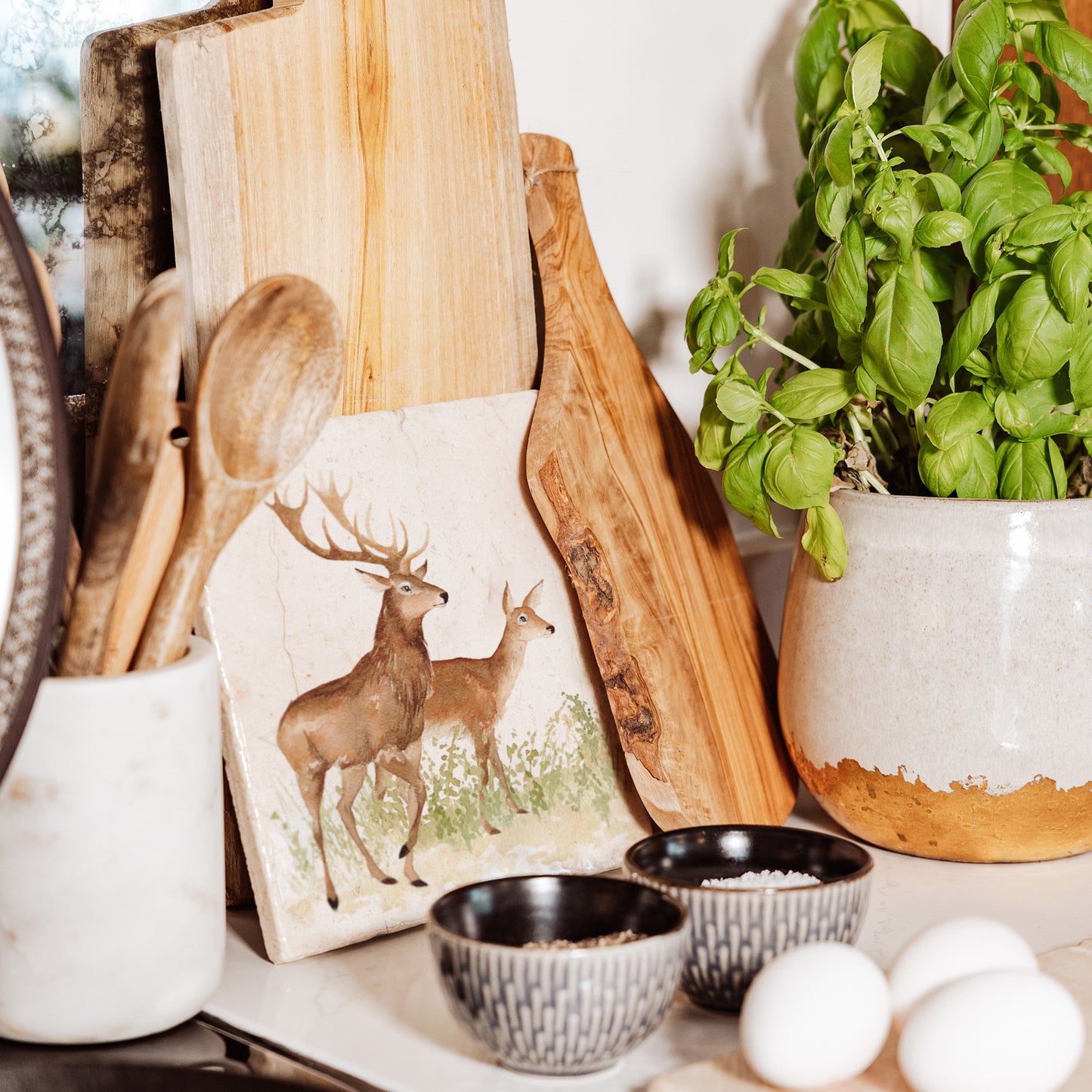 A medium marble cheese board propped up on a kitchen worktop. The cheese board features a red deer stag and hind in a watercolour style.
