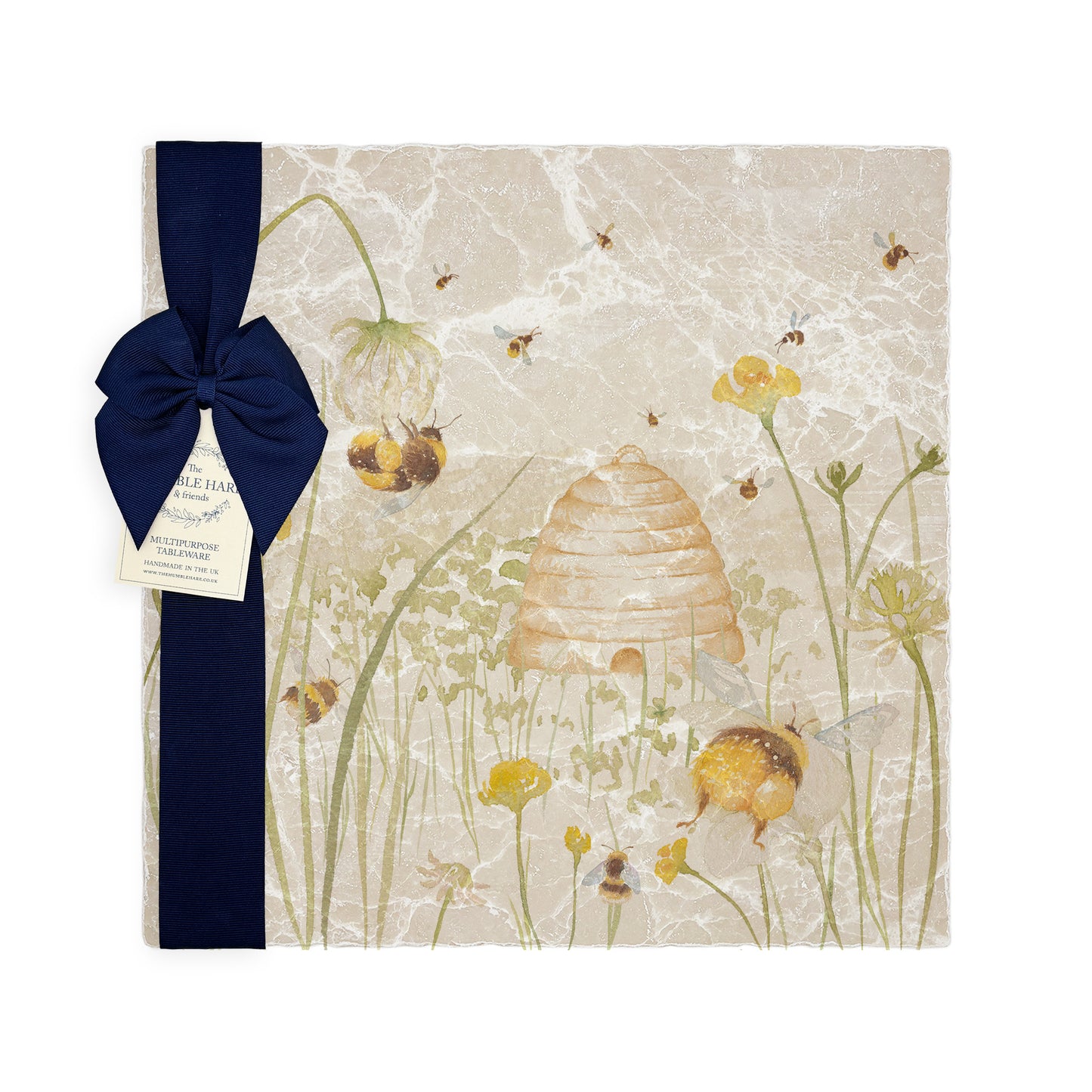A multipurpose marble platter with a watercolour design featuring bees and a beehive in a buttercup meadow, packaged with a luxurious dark blue bow and branded gift tag.