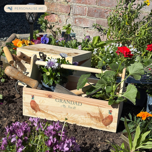 wooden luxury Trug/Caddy the perfect personalised gift. Each product is lovingly designed, handmade with our Countryside inspired watercolour designs. This design features Vibrant Male pheasants and a lady pheasant in a farmers field, the trug is pictured in a flower bed unique designs for a truly one off special occasion for a loved one.