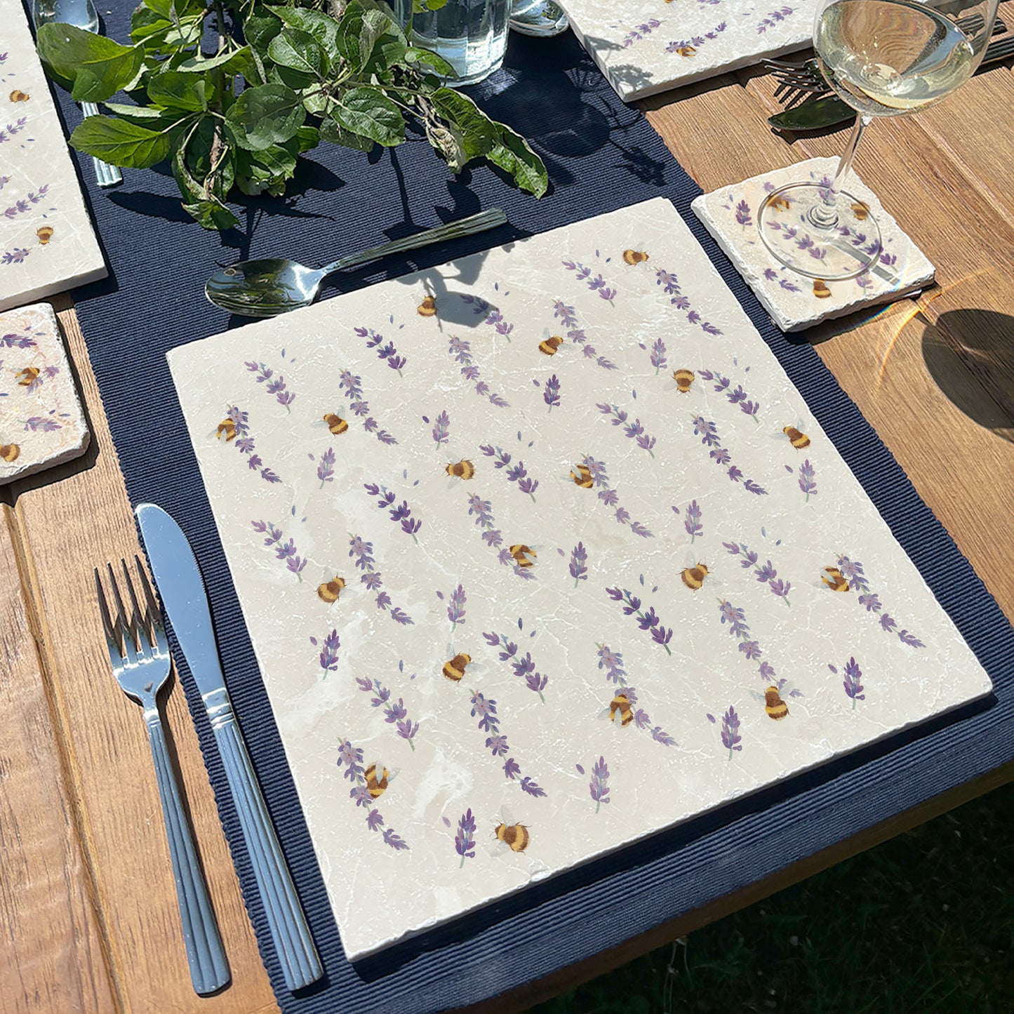 An garden dining table set with large marble placemats featuring a watercolour pattern of busy bees and lavender flowers.