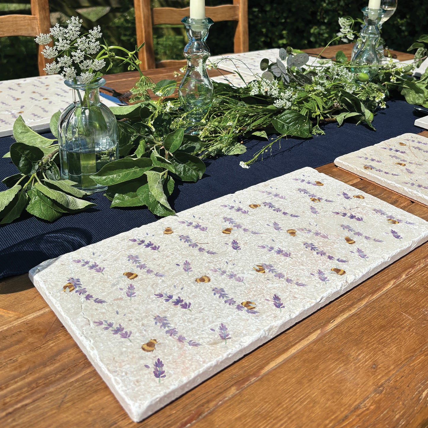A rectangle grazing board set on an outdoor table. The platter is decorated with a watercolour pattern of bees and lavender.