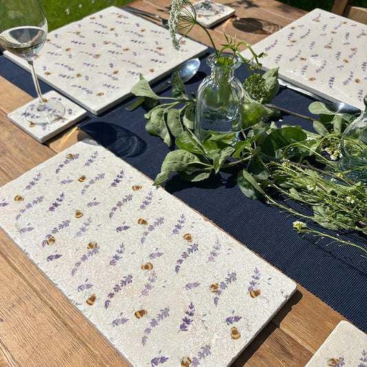 A handmade marble sharing platter set on a garden dining table. The platter features a watercolour pattern of bees and lavender flowers.