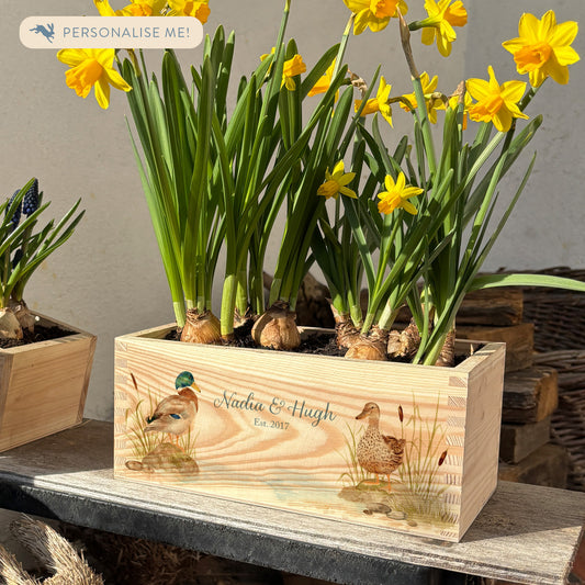 A rectangle wooden planter full of bright daffodils. The planter box shows a watercolour design of two mallard ducks by the pond, and is personalised with a special message and custom names and anniversary date. An ideal gift for gardeners, wedding, anniversary and engagements.