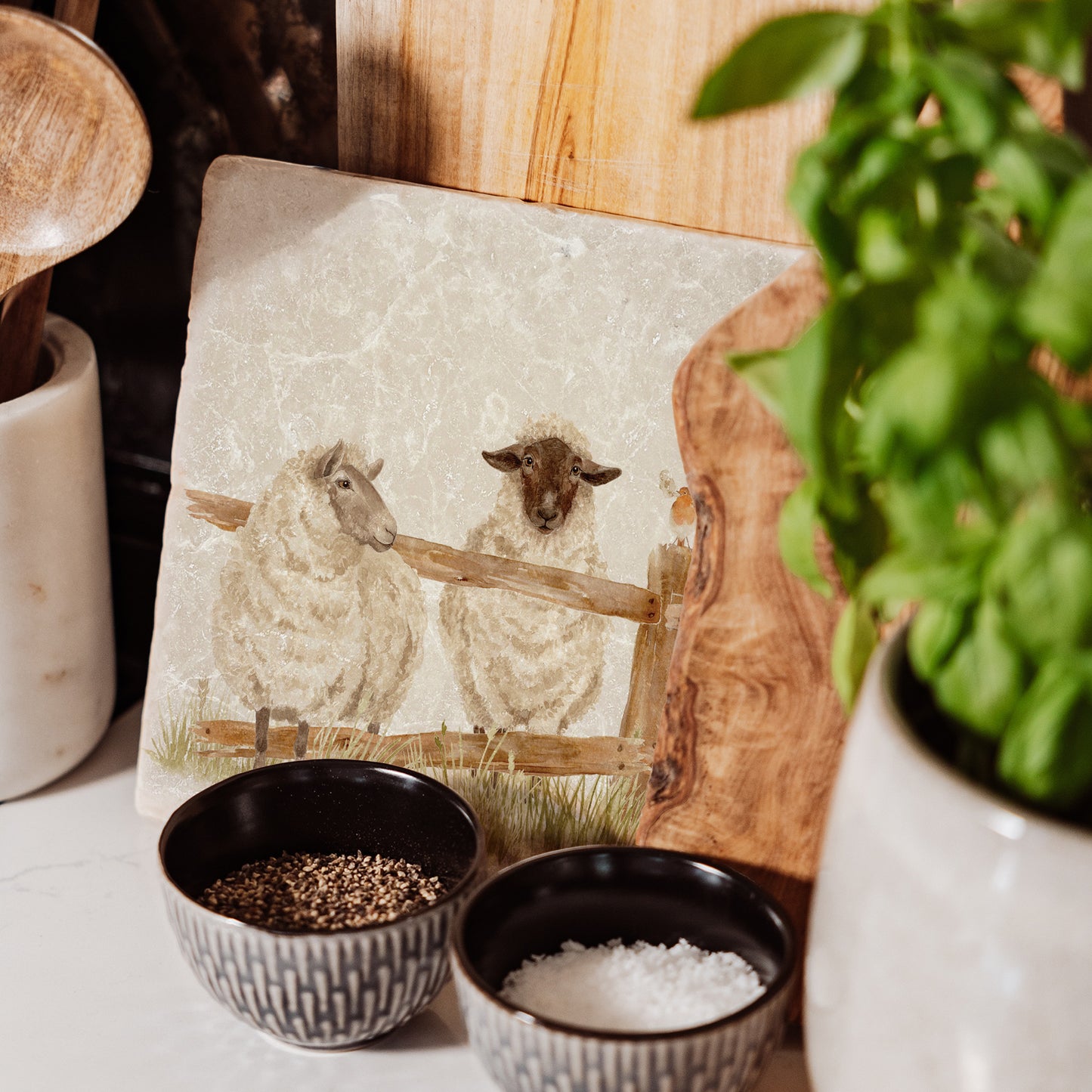 A handmade medium marble platter featuring a watercolour design of two sheep escaping from their field through a broken fence. The platter is propped up on a kitchen worksurface.