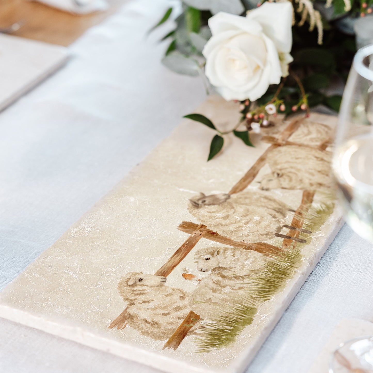 A handmade marble sharing board featuring a charming watercolour design of sheep escaping from their field. The platter is set on a dining table as a serving board.