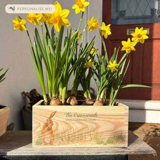 A rectangle wooden planter full of bright yellow daffodils. The planter box shows a watercolour design of The Humble Hare in grass, and is personalised with a special message and custom family name and love message. A perfect gift for weddings, anniversaries or engagements.