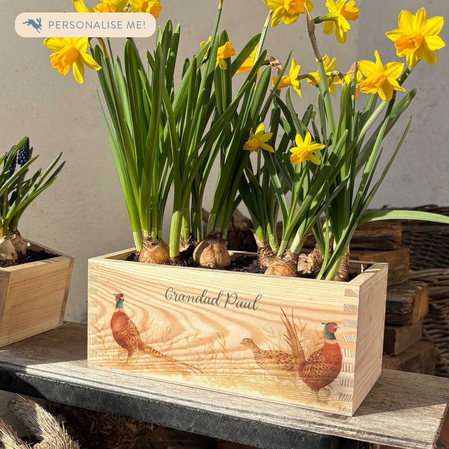 A rectangle wooden planter full of bright daffodils. The planter box shows a watercolour design of pheasants in a field, and is personalised with a special message and custom name. An ideal gift for gardeners or special occasions.