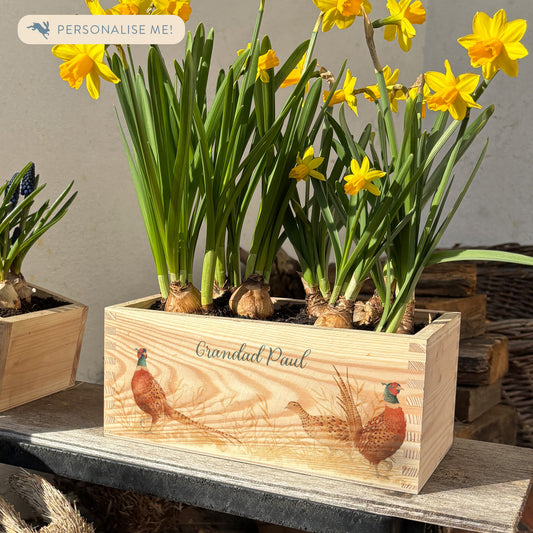 A rectangle wooden planter full of bright daffodils. The planter box shows a watercolour design of pheasants in a field, and is personalised with a special message and custom name. An ideal gift for gardeners or special occasions.