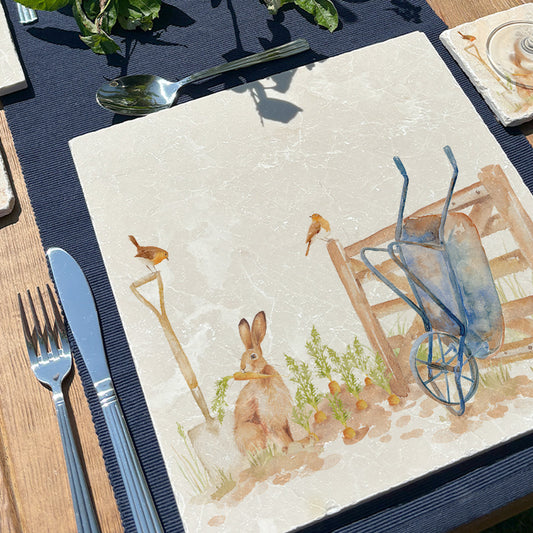 A garden table set with square cream marble placemats featuring a watercolour vegetable patch design.