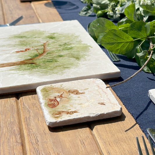 A square marble coaster featuring a watercolour scene of rabbits and a fawn.