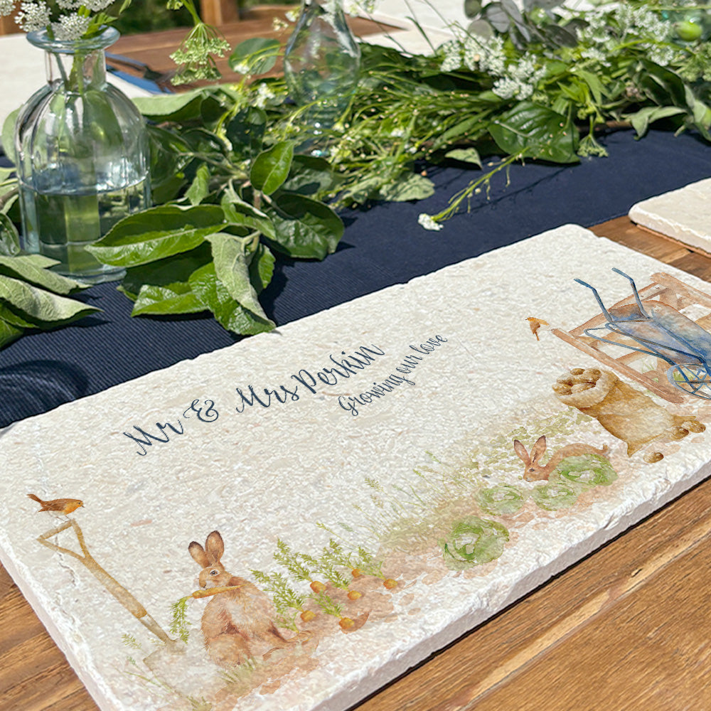 A personalised marble platter with hares and robins in a vegetable patch. It is personalised with a couple's name and 'Growing our love' in dark blue calligraphy.